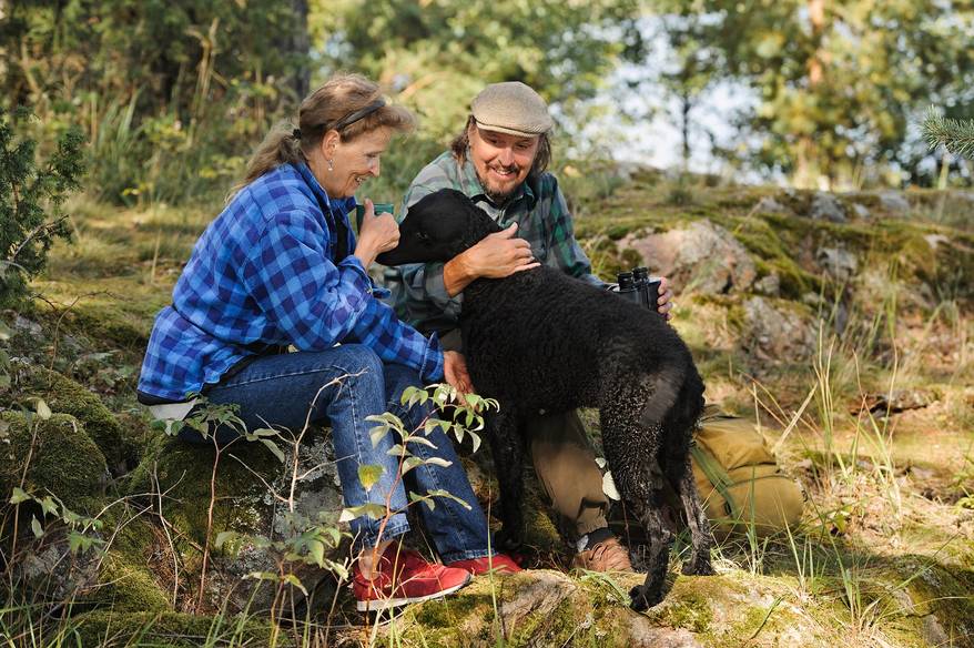 Senior couple playing with their pet dog while out hiking. The dog is a curly haired retriever.